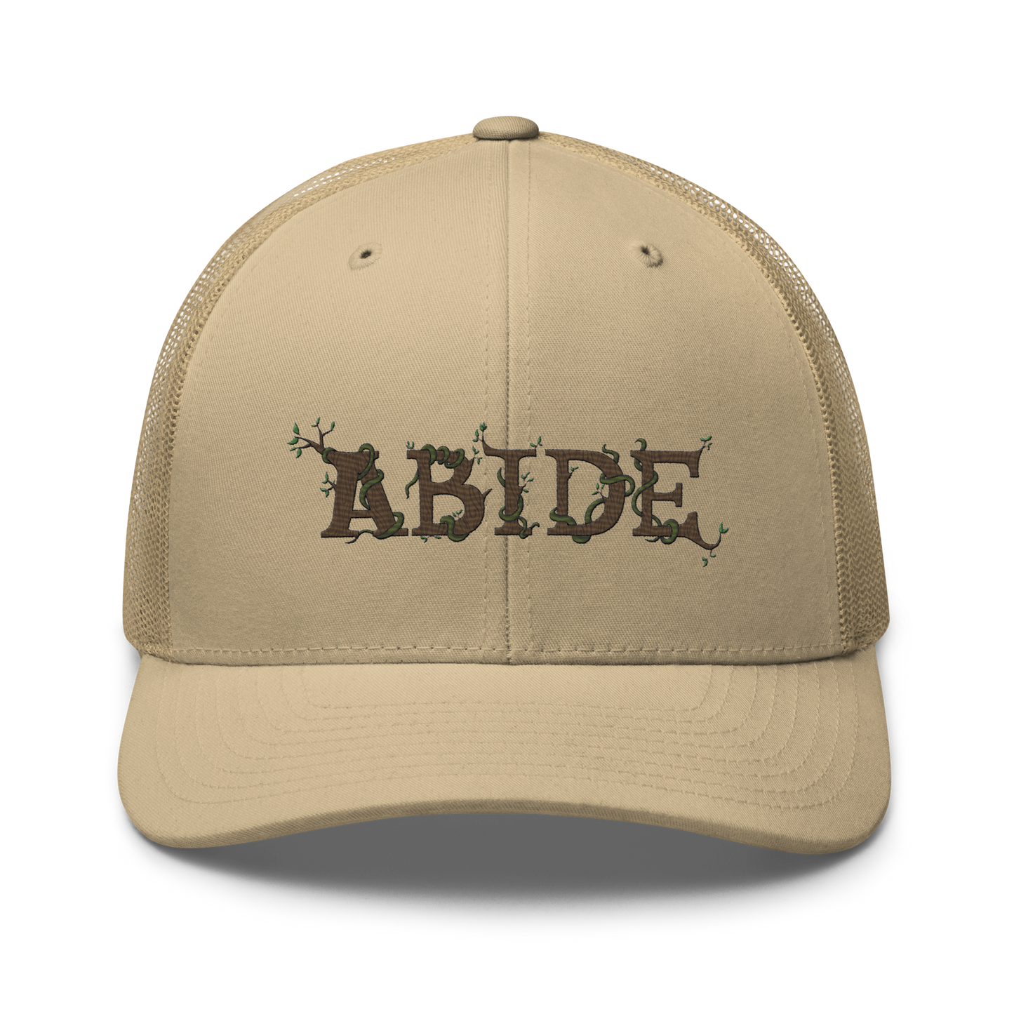 Desert tan trucker hat with the letters Abide on the front. The letters are in brown with green vines wrapped around. The Abide is embroidered on the hat.