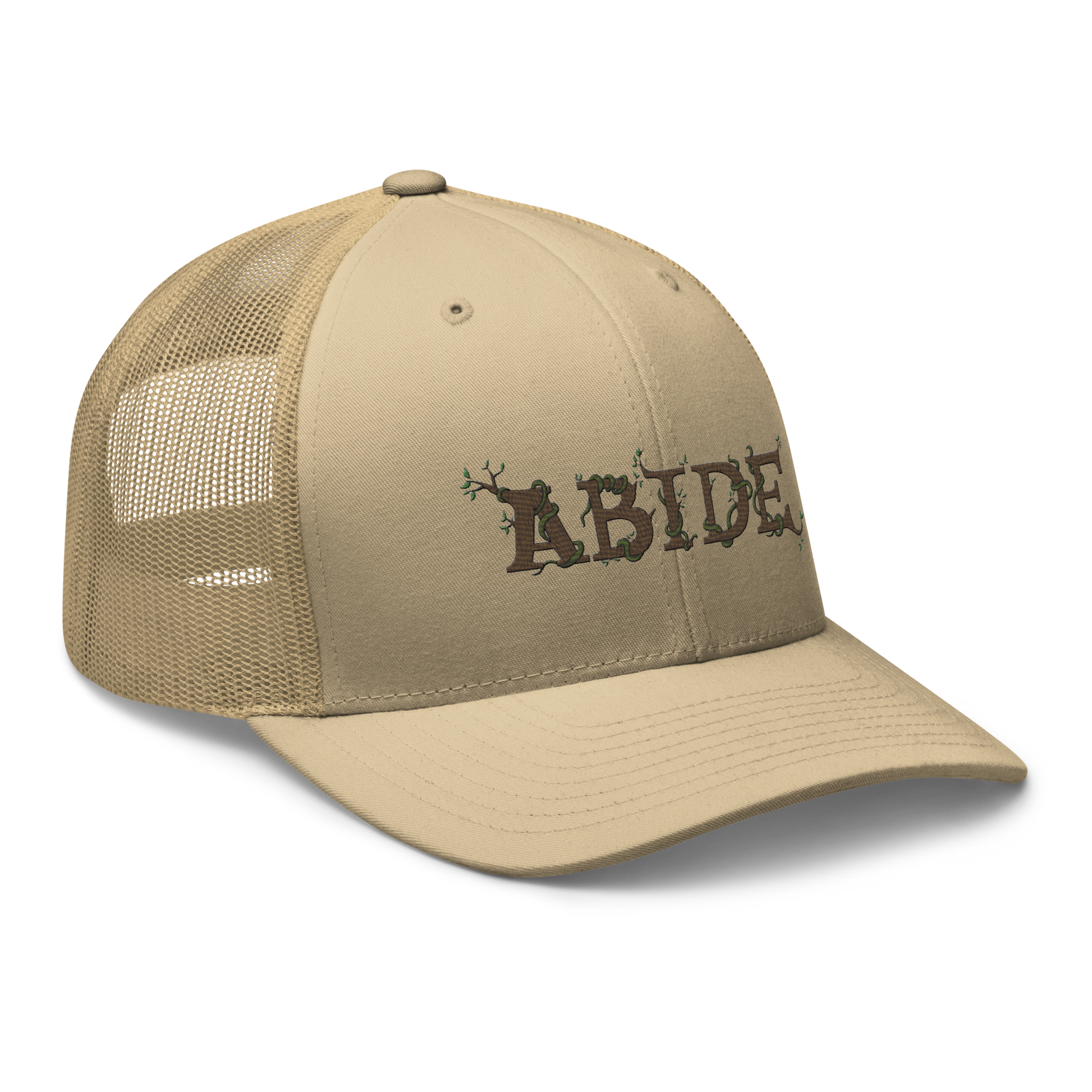 Desert tan trucker hat with the letters Abide on the front. The letters are in brown with green vines wrapped around. The Abide is embroidered on the hat.